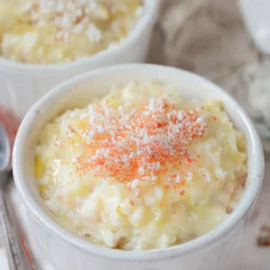 A creamy bowl of Rizogalo, Greek rice pudding, topped with a sprinkle of cinnamon. The dish features a rich, velvety texture and is garnished with lemon zest, showcasing the classic flavors of this comforting dessert.